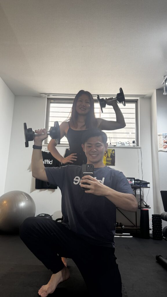 女性とダンベルを持ってポーズする男性トレーナー
